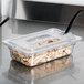 A Carlisle clear plastic container lid with food in it on a counter with a spoon notch.