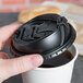 A hand holding a Dart black Optima lid over a white coffee cup.