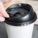 A hand using a black Dart Optima lid to close a coffee cup on a counter.