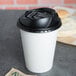 A white Dart paper hot cup with a black Optima lid on a table.