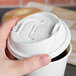 A hand holding a white plastic cup with a Dart white Optima lid and reclosable tab.