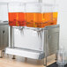 A Crathco refrigerated beverage dispenser with two containers of orange liquid.
