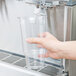A hand holding a clear plastic cup under a Crathco beverage dispenser.