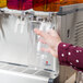 A person using a Crathco Simplicity Bubbler refrigerated beverage dispenser to fill a plastic cup.