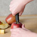 A hand using a Victorinox apple corer with a black handle to core an apple.