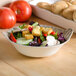 A melamine bowl of salad with croutons and tomatoes on a table.