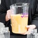 A woman using a Cambro purple measuring cup to pour orange juice.