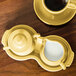 A yellow Fiesta sugar and creamer tray set on a wood table with a cup of coffee and saucer.
