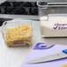 A clear plastic Cambro food storage container with pasta and a knife on a counter.
