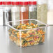 A Cambro clear polycarbonate container with pasta in it on a counter in front of spices.