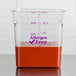 A Cambro clear polycarbonate food storage container on a counter with red liquid inside.
