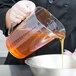 A person in a chef's uniform pouring purple liquid into a measuring cup.