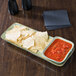A rectangular Tuxton china bowl filled with chips and salsa on a table.