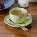 A TuxTrendz Artisan Sagebrush saucer with a spoon on it next to a cup of tea.