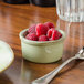 A Tuxton Artisan Sagebrush ramekin filled with raspberries on a table.