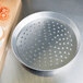 An American Metalcraft perforated aluminum pizza pan with a pizza crust on it.