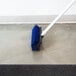 A blue Carlisle Hi-Lo floor scrub brush with squeegee being used on a floor.