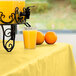 A glass of orange juice sits on a table with a Mimosa Yellow plastic table cover.