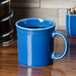 A blue Fiesta Java Mug with a white stripe and a handle filled with a drink on a table.