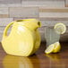 A yellow Fiesta disc pitcher filled with water and lemons on a wood surface.