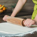 A person rolling out dough with an Ateco maple wood rolling pin.