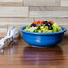 A blue Fiesta serving bowl filled with salad on a wooden table.