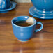 A blue Fiesta china cup with tea in it and a tea bag on a table.
