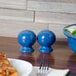 A blue Fiesta salt shaker on a table with a bowl of salad.