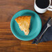 A slice of pie on a Fiesta® turquoise appetizer plate next to a cup of coffee.