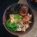 A bowl of ramen with mushrooms and greens topped with Kikkoman Traditionally Brewed Soy Sauce.