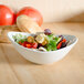 A Tuxton white porcelain bowl filled with salad with croutons and tomatoes on a table.