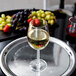 A customizable Tritan plastic tall wine glass filled with white wine on a tray with grapes and fruit.