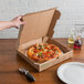 A hand uses a GreenBox pizza box with built-in plates to cut a pizza on a table.