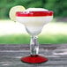 A Libbey Aruba margarita glass with a drink on it, with a red rim and base, filled with a margarita and garnished with a lime.