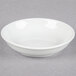 A Tuxton bright white china bowl with an embossed rim on a grey surface.