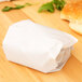A white wax paper wrapped sandwich on a wooden table.