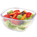 A salad in a clear square bowl with tomatoes, lettuce, and carrots.