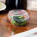 A salad in a clear plastic square bowl.