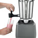 A person pouring pink liquid into a Waring food blender.