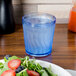 A blue Dinex SAN plastic tumbler filled with water next to a plate of salad on a table.
