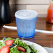 A blue Dinex SAN plastic tumbler filled with water next to a plate of salad.