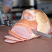 A person using a Waring cordless electric knife to cut ham on a cutting board.