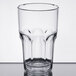 A close-up of a clear plastic Dinex tumbler with a rim on a table.