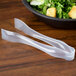 A pair of Visions clear plastic tongs next to a bowl of salad.