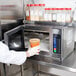 A person in a white glove using a Waring commercial microwave to heat a plastic container of orange liquid.