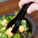 A person using Visions black disposable plastic tongs to serve croutons onto a salad.