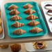 A green Cambro market tray filled with pastries and muffins on a bakery display counter.