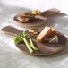 An Elite Global Solutions round faux driftwood serving board with cheese and crackers on it.