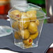 A clear plastic container of green olives on a table.