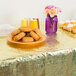 A gold plastic table cover on a table with a plate of doughnuts and cupcakes.